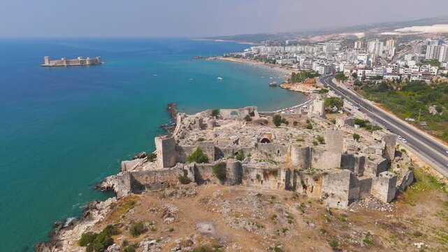 Kizkalesi, Mersin, Turkey. Aerial view of Korykos Castle stone ruins on a Mediterranean peninsula under clear summer sky, with coastal town and Maiden Castle island in the distance.. Aerial View