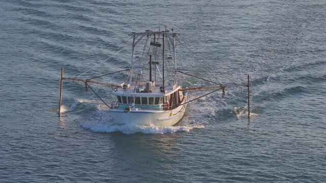 Commercial Shrimp Trawler Cruising On Water, Leaving Wake With Extended Outriggers. drone shot
