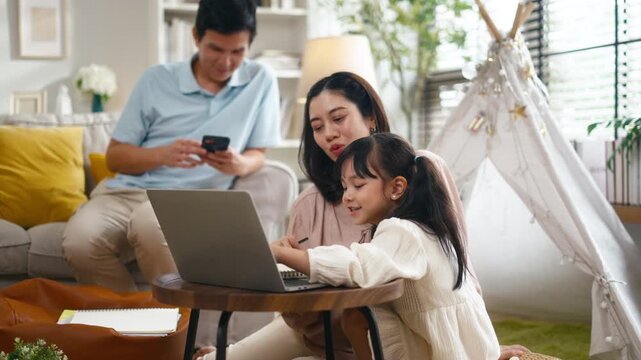 Happy Asian family father teaching daughter drawing on easel while mother giving support at home. Parents homeschooling little girl during summer break or back to school season for child development