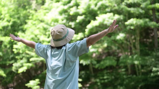 森林浴を楽しみながら深呼吸で両手を広げる女性　アウトドアや夏のキャンプを楽しむ顔無しの後姿イメージの動画