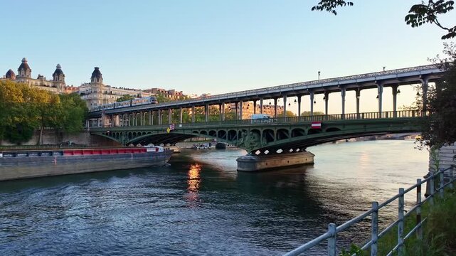 Barge passes under Pont de Bir-Hakeim bridge as metro train crosses over it during beautiful sunrise on Seine river in Paris, France