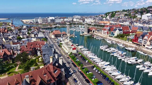 Sailboats and yachts moored in marina of seaside resort town of Deauville in Normandy, France. Aerial forward