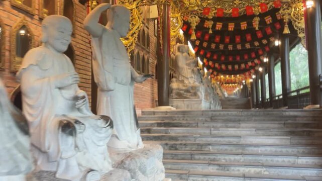 Indoor corridor at Bai Dinh Pagoda in Ninh Binh Vietnam featuring white stone Arhat statues beside temple stairs and colorful hanging flags.