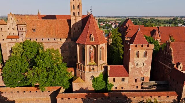 Drone reveals medieval Malbork fortress glowing beneath warm sunrise over Poland
