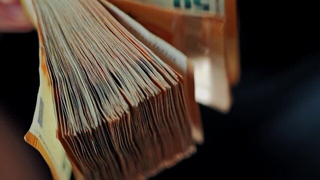 Slow motion closeup reveals flipping stack of fifty euro banknotes in darkness.