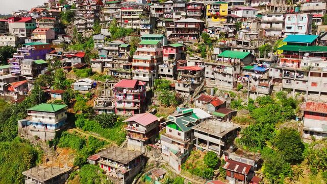 Warm daylight aerial reveals layered hillside homes across dense Baguio area