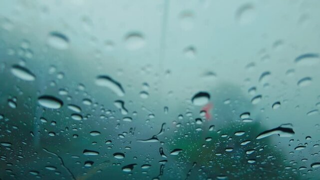 Blurred vehicle lights glow softly through rain covered windshield in traffic