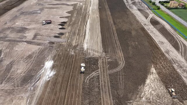 Large scale terrain preparation and compaction activity near motorway junction infrastructure in the Po Valley, Italy with graded corridors, heavy machinery and engineered transport development, aeria