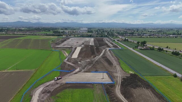 Drone flyover above large scale logistics and transport infrastructure development near the Fiorenzuola d'Arda motorway interchange with the northern Apennines in the background.