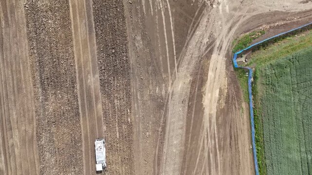 Pneumatic roller compactor operating across stabilized terrain during freight infrastructure preparation with visible grading lines and engineered soil textures, top down drone shot.