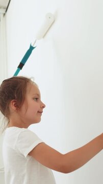 A mother and her young daughter are painting a white wall together, using paint rollers and enjoying a home renovation project