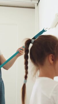 A mother and her young daughter happily paint a white wall together with rollers, enjoying a home improvement project
