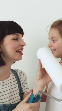 A mother and her young daughter share a joyful moment while holding a paint roller, preparing to redecorate their home