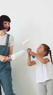 A mother and her young daughter are holding paint rollers, ready to redecorate a room with a fresh coat of paint
