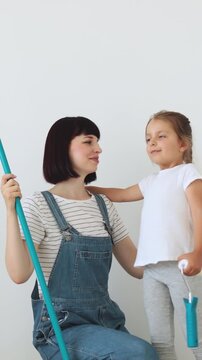 A mother and her young daughter smile while holding a paint roller, ready to redecorate their home
