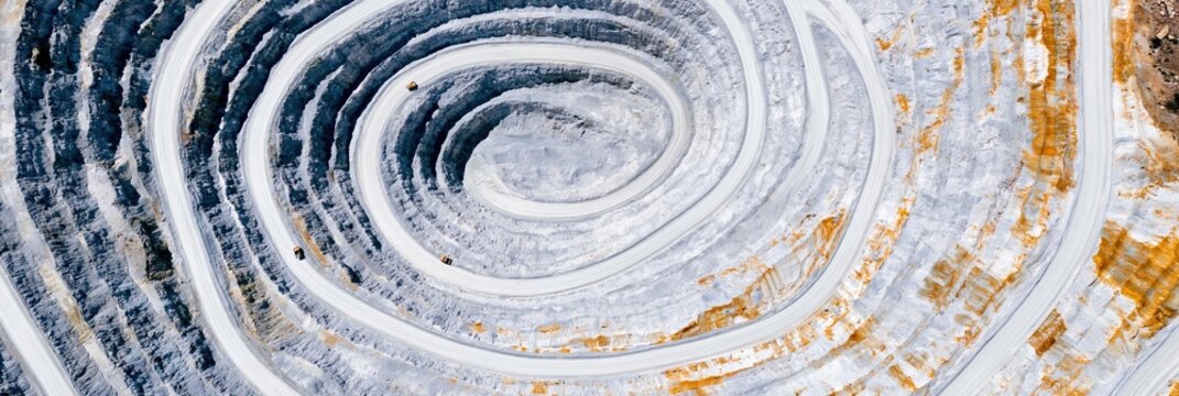Massive open-pit mine aerial view with spiraling concentric circular terraces for heavy industry reports, mining sector advertising and extraction site concepts