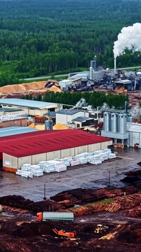 Aerial vertical reveal of stacked log piles wood chips and lumber at Stora Enso sawmill timber factory surrounded by forest in Latvia