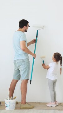 A father and his young daughter are painting a white wall together with rollers, creating a shared memory during home renovation