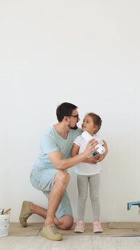 A father and his young daughter are having fun while painting a room, sharing a moment of joy and connection