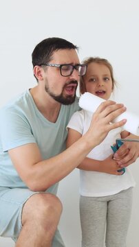 A father and his young daughter are enthusiastically painting a wall together, holding a paint roller and sharing a moment of fun