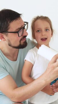 A father and his young daughter are holding a paint roller, seemingly discussing or preparing to paint a wall