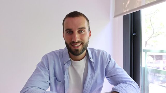 Young handsome man with a beard talking to the camera and gesturing during a video conference, smiling and looking at the webcam for an online job interview or a virtual meeting with friends