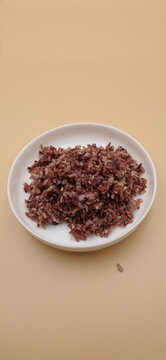 Steamed organic black riceberry in a white ceramic plate on a beige background.