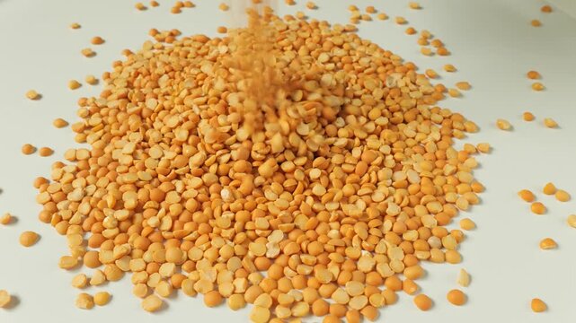 Yellow split peas pouring into a pile on white background