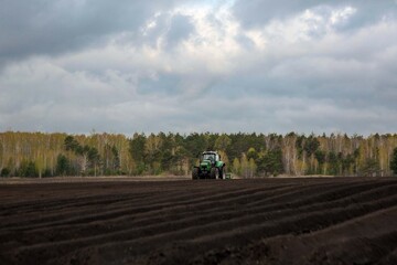 Naklejka premium A tractor plowing a field in spring. Agricultural work, farming.