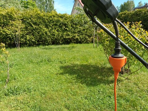Outdoor electrical safety concept. Orange power extension cord connected to a lawn mower on a green grass backyard, closeup detail.