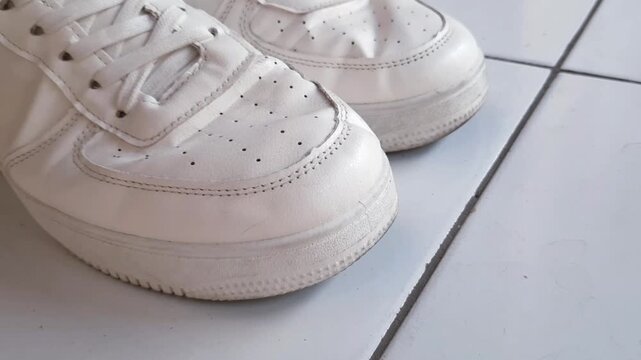 Close up shot of a person bending their feet alternately, showing prominent creases forming on white leather sneakers.