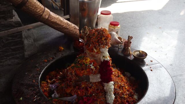 Raw video footage of holy water flowing from a brass pipe onto a decorated Shiva Lingam inside a Hindu temple in Uttarakhand India during worship ritual.