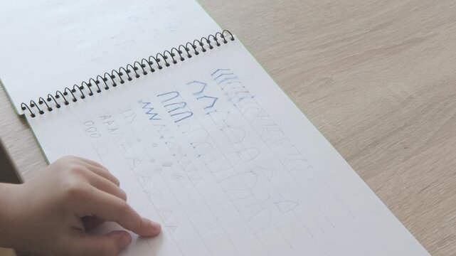 Close up preschool kid hand writing letter elements in notebook, practicing handwriting strokes, early literacy and school preparation concept, Developing fine motor skills and hand-eye coordination