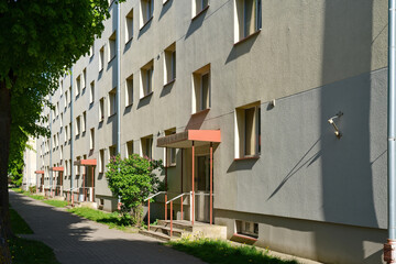 Fototapeta premium Facade of a typical panel apartment building with several entrances and a sidewalk on a sunny day. Eastern European residential district, real estate and housing concept.