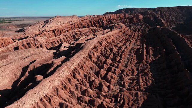 Panoramic aerial over dramatic eroded salt rock badlands with sharp ridges and deep ravines of the Cordillera de la Sal under vivid blue sky. Valle de la Muerte, Chile