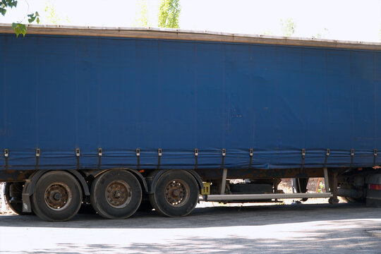 Side view of blue semi truck trailer parked on asphalt road. Large cargo container for vehicle logistics. Transport industry, freight delivery and commercial shipping business concept.