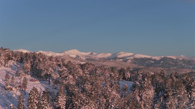 Mount Blue Sky spring pink morning sunrise alpenglow Denver Front Range Rocky Mountains Mt Evans Evergreen Colorado aerial drone landscape snowy forest trees valley rolling hills to the right motion