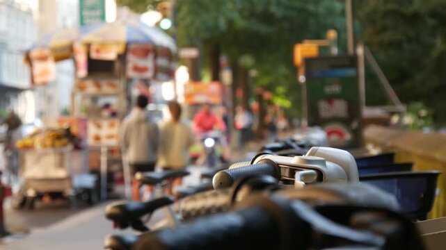 Manhattan Midtown street New York City, United States. Rental bicycle parking, Central Park West summer trees greenery. Bike for rent in row. People pedestrian on sidewalk pavement. Hot dog fast food
