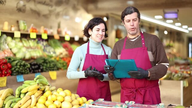 Man and woman staff in apron hold paper documents in hands, counts and records quantity of goods on display in store. Seller take inventory of goods, checks actual availability with documentary report