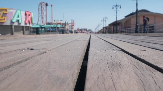 Coney Island beach promenade in Brooklyn, New York, United States. Wooden boardwalk near retro luna park. Amusement park on ocean coast beach. Waterfront summer holiday, people walking on promenade