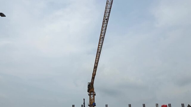 Low angle view of a tall yellow construction tower crane jib extending diagonally across a pale cloudy overcast sky.