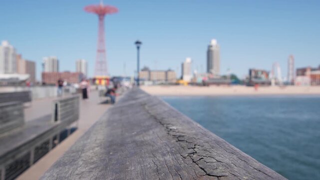 Coney Island beach, wooden pier promenade in Brooklyn, New York, United States. Boardwalk near retro luna park. Amusement park on ocean coast beach. People on waterfront summer holiday in NYC, USA