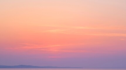 Fototapeta premium Beautiful sunset sky with soft pastel colors, shades of orange, pink and purple over a calm sea with a distant coastline silhouette