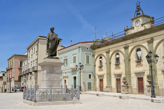 Horace statue standing in Piazza Orazio in Venosa, Italy. Horace statue overlooking Piazza Orazio, surrounded by historic buildings and blue sky.