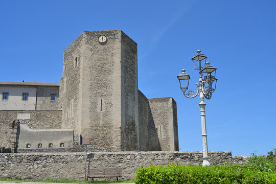 Melfi castle tower and historic street lamp. Castello di Melfi castle stone tower with clock and a vintage street lamp under a clear blue sky.
