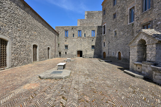 Melfi Castle courtyard showing historic stone architecture. Historic Castello di Melfi Castle courtyard with ancient stone walls and herringbone brick paving under a blue sky.