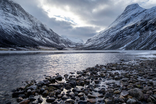 A beautiful cloudy day at a mountain lake with stone pebbles on the shore. A winter scenery on Eidsvatnet in Norway, Geiranger area, UNESCO world heritage site.