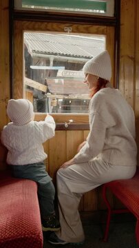 Vertical Screen: A young mother and her little boy look out the window of the train as it pulls into a tourist station. They enjoy the view of the surroundings and the arrival.