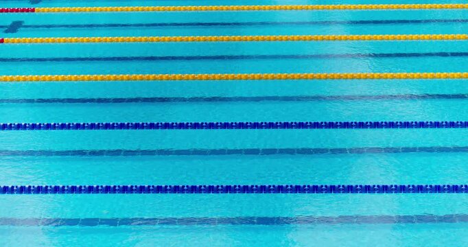 Empty olympic swimming pool lanes with blue and yellow float dividers and clear water ripples