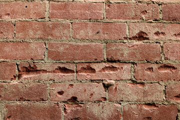 Obraz premium A full-frame, damaged texture of a red brick wall. The surface displays wear, pits, missing chunks, and holes.